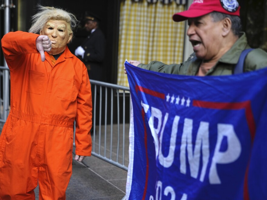 Mike Hisey, left, wearing a mask of former President Trump in a prison uniform while Mariano Laboy, right, holds a Trump reelection sign outside of Trump Tower on Tuesday, March 21, 2023, in New York.