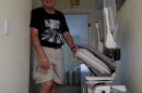Howard Weinberg, a retired physician living with Parkinson’s disease, stands beside a stair lift at his Virginia Beach home.