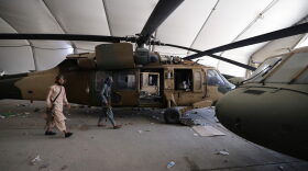 Taliban fighters walk past damaged Afghan Air Force helicopters at a hangar at the airport in Kabul.