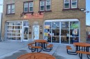 The exterior of the Sherman Park Grocery Store features several round orange lunch tables on its patio.