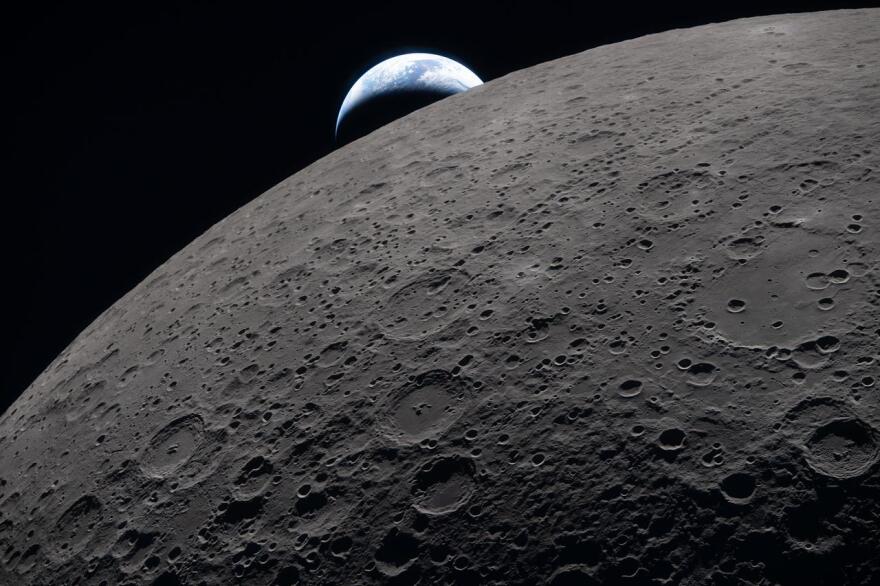 The lunar surface fills the frame in sharp detail, as seen during the Artemis II lunar flyby, while a distant Earth sets in the background. This image was captured at 6:41 p.m. EDT Monday, just three minutes before the Orion spacecraft and its crew went behind the moon and lost contact with Earth for 40 minutes before emerging on the other side.
