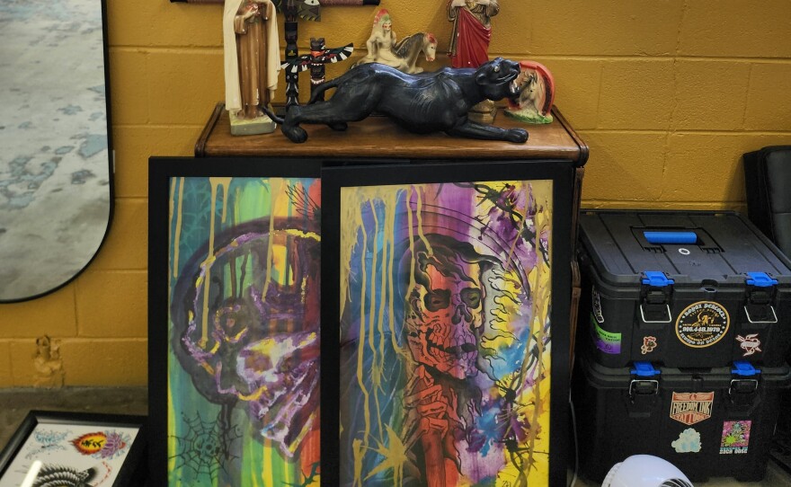 Various statious, some religious, sit on a table above colorful artwork.