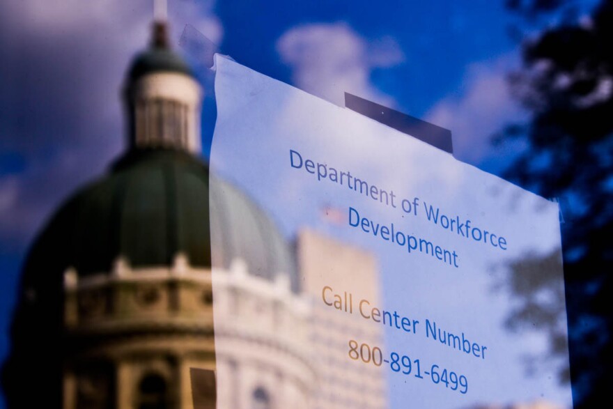 The Indiana Statehouse reflected in a window giving contact information related to unemployment benefits.