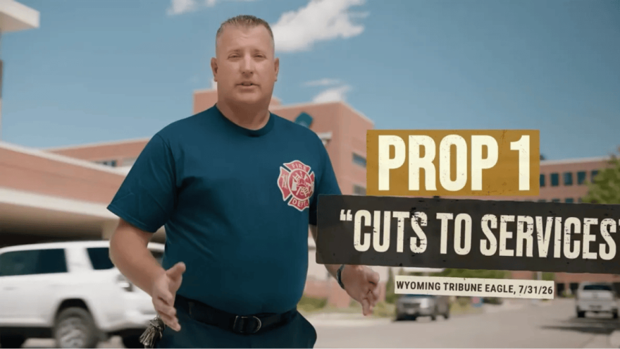 A men wearing a shirt with a logo of a fire department stands in front of a building. Words are superimposed over the image reading, "Prop 1 'Cuts to services' Wyoming Tribune Eagle, 7/31/26."