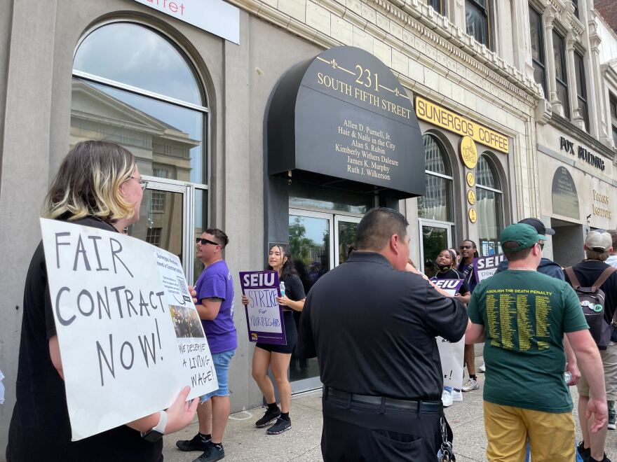  People march and protest outside Sunergos Coffee's South Fifth Street location. One person holds a white sign that says 'Fair Contract Now!' in black letters.