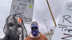 A picketer is seen with a scary doll mask. Another protester holds a sign that says "zombies for fair treatment." 