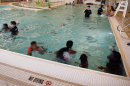 Children lined up near the edge of a large swimming pool as an instructor stands in the water