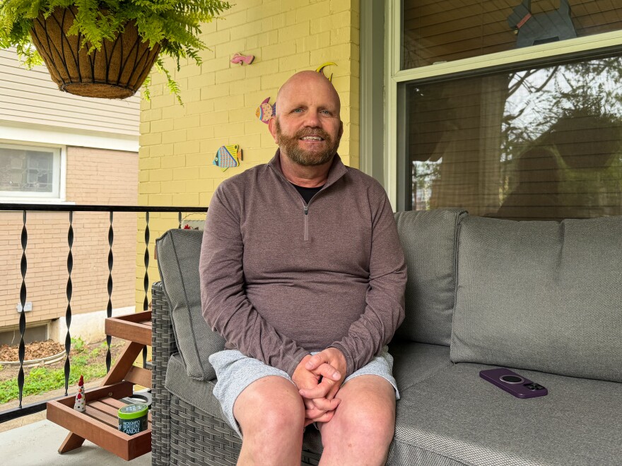 A man sits on a couch on his patio and poses for a photograph.