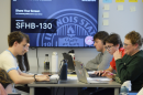Students use laptops while they sit together at a tall table.