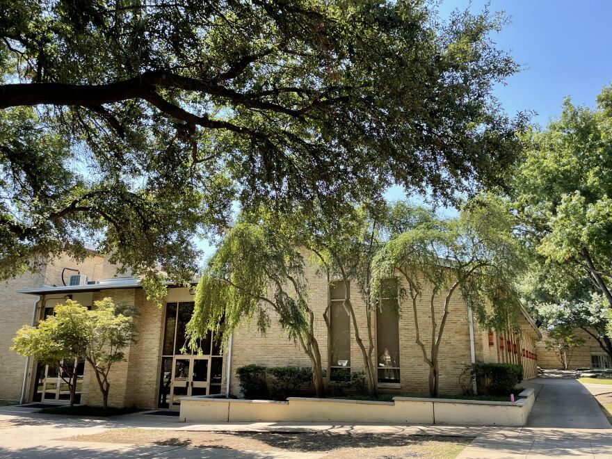 A sunny, exterior shot of a school, covered in trees.