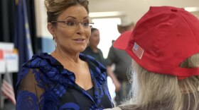 woman in print shirt greets another woman wearing a red cap.