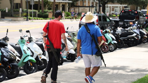 Two men who appear to be armed with rifles walk across from Tigert Hall, where protesters gathered, followed by a UFPD officer, in Gainesville Fla., Wednesday, Sept. 9, 2026. (Julianna Bendeck/WUFT News)
