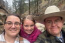 Tara Benson, Grace Benson and Jake Benson are framed together in a family photo with a mountainous background with green trees. 