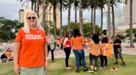 Woman in an orange shirt stands in Curtis Hixon Park in downtown Tampa at a gun violence awareness rally.