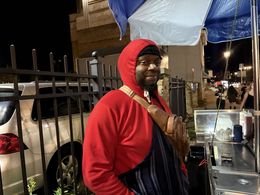 Photo of a man standing next to his hot dog stand