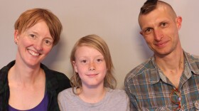 Portrait of a three member family from the chest up: Judith Rognli stands smiling and leaning her head toward her son Felix. Next to Felix, and also leaning his head toward him is his father Pete Rognli.
