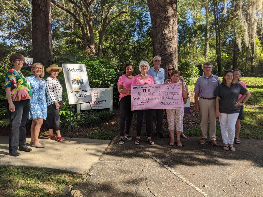 Several women stand outside holding an enlarged check.