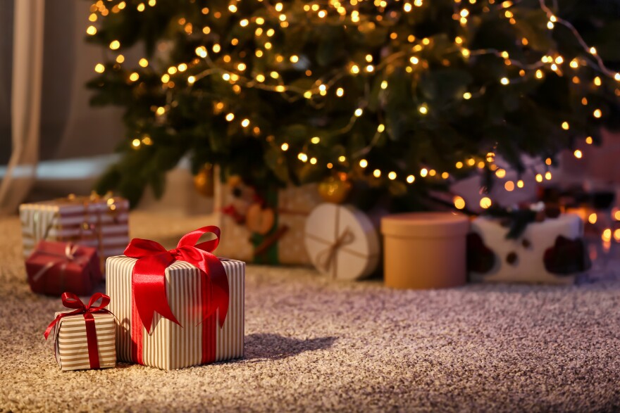 Beautiful Christmas gift boxes on floor near fir tree in room.