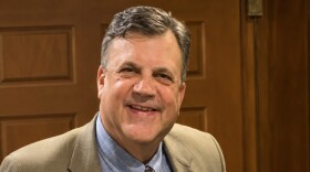A man smiles at the camera. He's wearing a suit.
