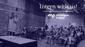 Someone stands on a stage, speaking into a microphone, in front of a crowd of people.