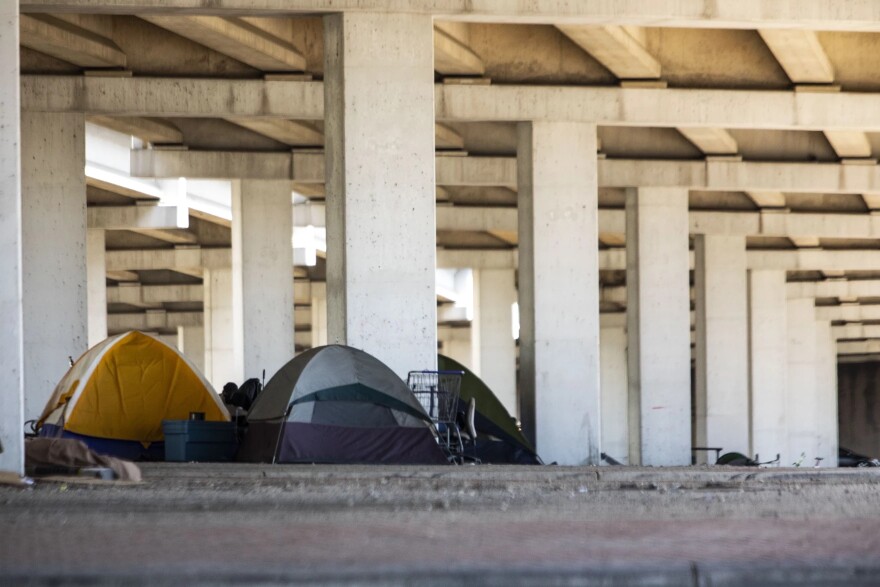 Tents are set up under a highway overpass.