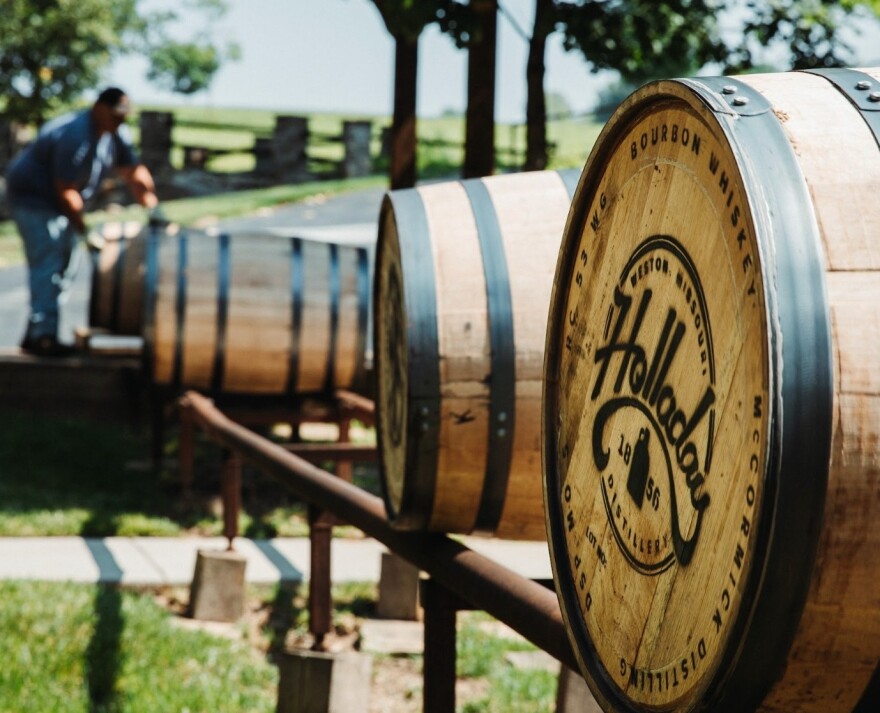 Wooden barrels with the logo for Holladay Distiller branded on them roll on a metal frame toward a man in the background. 