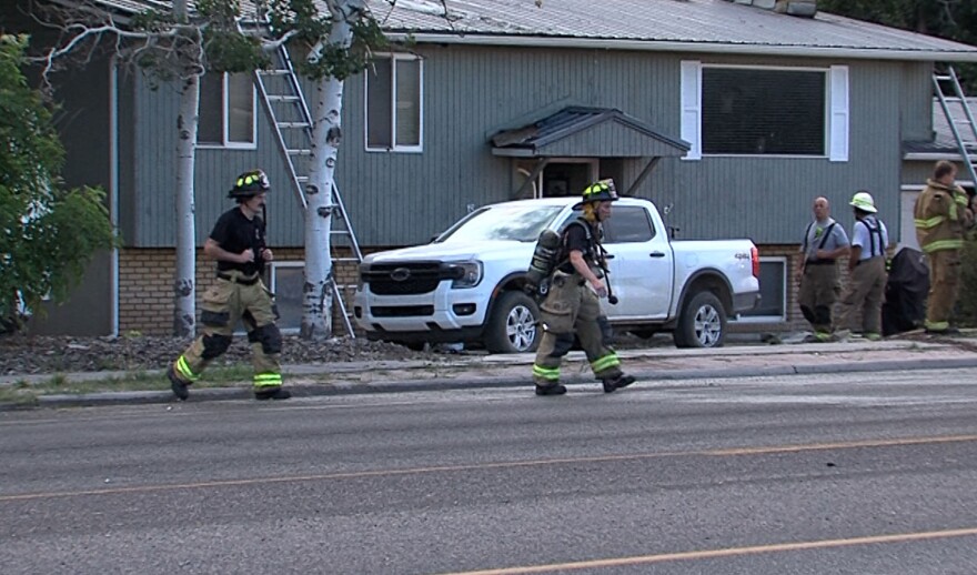 Firefighters walking away from a house with two ladders leaning on it. Three other men in firefighting gear are talking near the house.