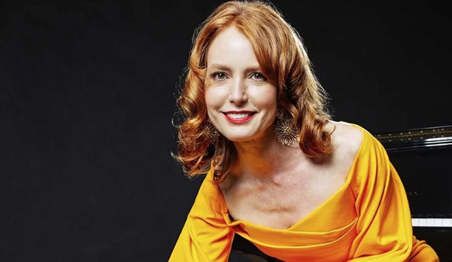 Woman with red hair in a yellow dress smiles at camera 