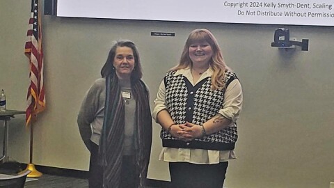 Two women pose for a photo in a conference room