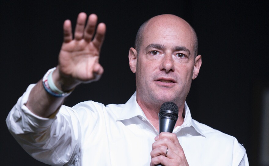 a man in a white shirt and black pants stands on a stage holding a microphone