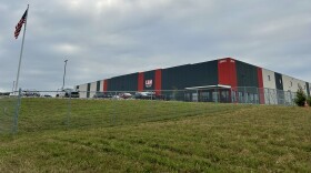 Photograph of L&M Fleet Supply distribution center with building, yard, fence, cars, and an American flag
