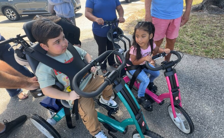 Marcel Rodriguez is 11 years old. He takes off on his new bike from Robbie’s Riders, Grampy’s Charities and Sanibel Captiva Community Bank. The three sponsors presented custom-made, adaptive bicycles and tricycles to local special needs children. Eight adaptive tricycles, worth nearly $3,000 each, were given out on Friday, March 20, 2026. Marcel has Duchenne muscular dystrophy, a genetic disorder that causes progressive muscle weakness. Liliana looks on.