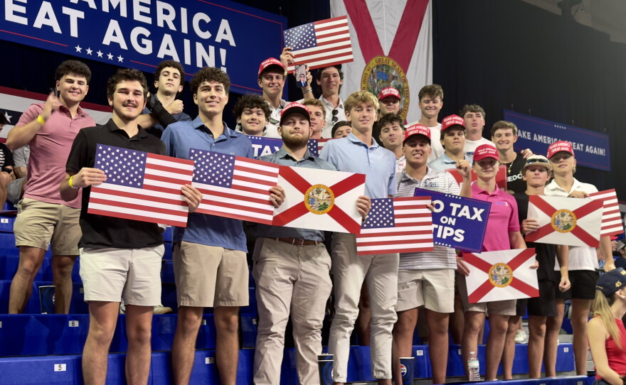 A group of young attendees show their support for the president with signs displaying the state flag, the American flag, and a few that read "NO TAX ON TIPS."