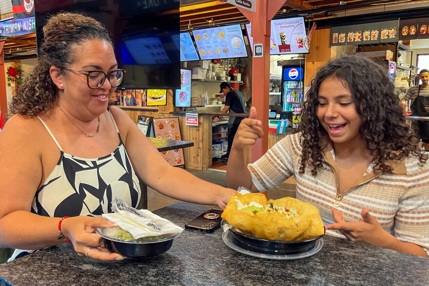 Mentee Esmeraida Figueroa (right) shares her excitement as her mentor Rebeca Carrasquillo places her lunch in front of her. The two shared lunch on September 19, 2026 at Parkville Market in Hartford. Sharing meals is one of their favorite ways of bonding, Figueroa and Carrasquillo said, along with attending sports games and trying out new activities.