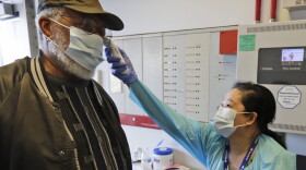 Registered Nurse Janice Tatonetti, right, takes the temperature of Harry Pearson before he votes in Ohio's primary election at the Cuyahoga County Board of Elections, Tuesday, April 28, 2020, in Cleveland.