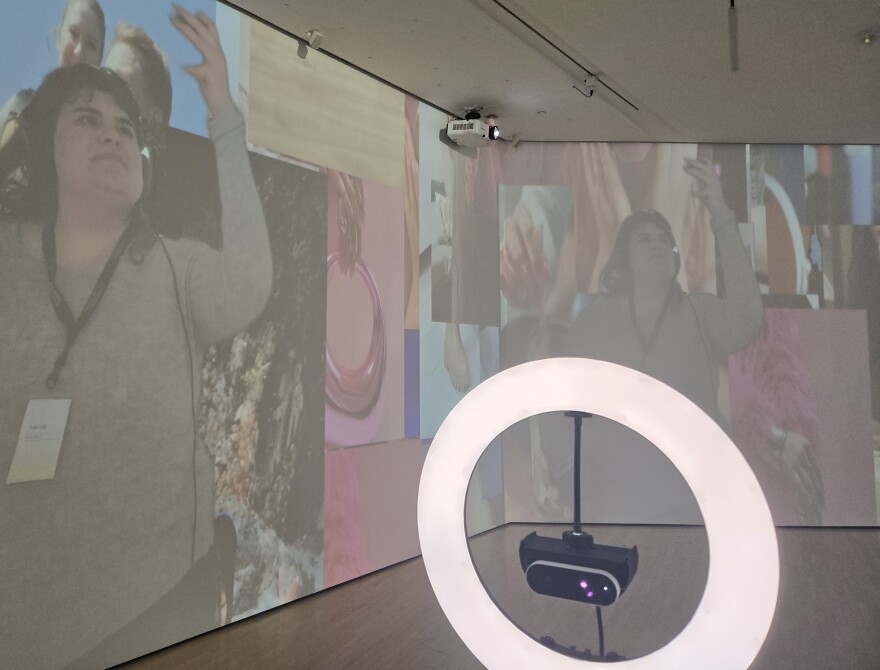 A ring light in the foreground, on the walls of the gallery space is projected images of WKAR's Sophia Saliby and social media videos