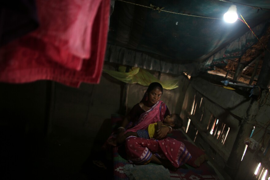 Arati Sardar sits in her house with baby Sridoy. One of the family's goats was taken and eaten by a tiger, but having electricity now helps keep the home safer.