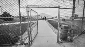 A chain link fence open to show two people walking away 