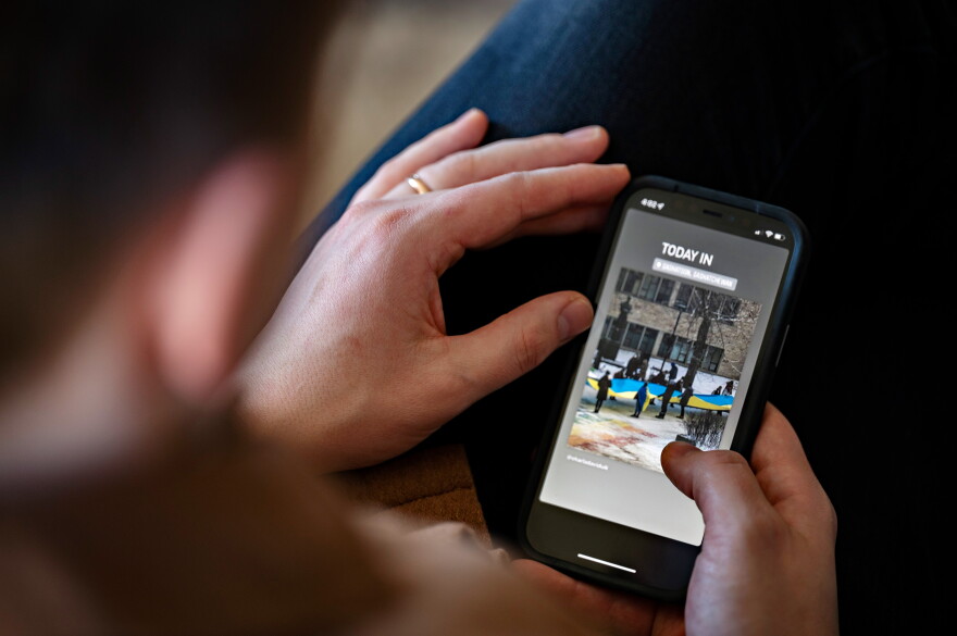 On his couch at home in New Haven, Vasyl Matsyuk looks through social media posts on his phone. He says it's odd seeing some of the photos out of Ukraine. People are going through horrific things, but they see a camera and some still smile.