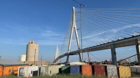 The Gordie Howe International Bridge across the Detroit River in a late stage of construction with multicolored shipping containers below, viewed from Detroit, Michigan in 2025.