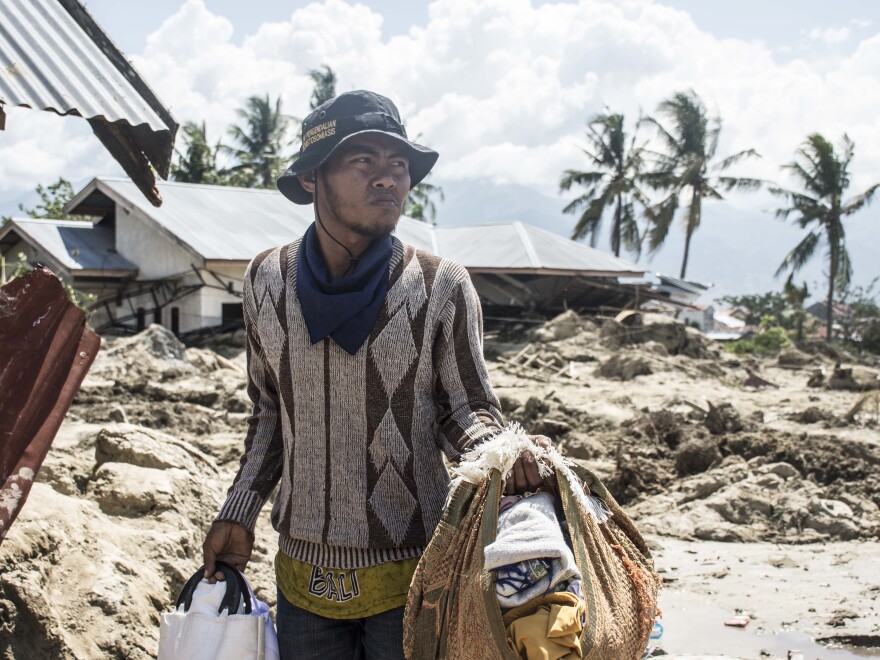 Afit Badrudin, 28, carries blankets and canisters as he shuttles between a makeshift camp and his destroyed home. He recalls standing at the cigarette stall fifty yards from his house when suddenly the earth began shaking horizontally, then vertically, and then gyrating as if "in a blender."