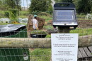 A sign posted to a fence announces the community garden hours in four languages.