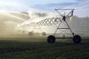 Sun shines through the spray of a crop irrigation system on an agricultural field. 