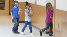 Students carry sack lunches as they walk through a hall, Tuesday, Feb. 2, 2021, at Elk Ridge Elementary School in Buckley.