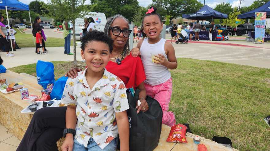 Grandmother wearing a red shirt sitting with her two grandchildren. 