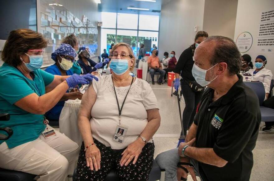 Ron Book (far right) Chairman of the Homeless Trust looks on as a medical staff vaccinates Janet Bristol, who got her second round of covid vaccines at Jackson Memorial as part of a partnership program between the Homeless Trust and the Jackson Memorial Hospital to vaccinate senior citizens who are homeless and/or housed in permanent housing. on Friday, February 19, 2021.