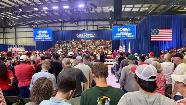 Many supports stand in a large venue with screens saying "Iowa Welcomes President Donald J Trump." 