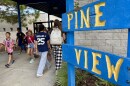 Close-up of a wooden blue and yellow sign that says Pine View with children walking to the left