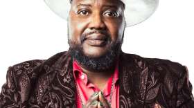 A man wearing a white cowboy hat, poses against a white background.