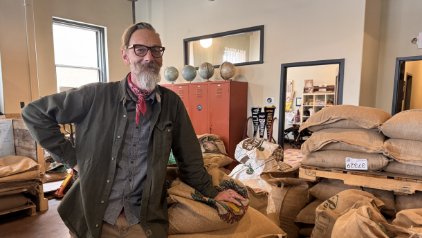 A man stands next to dozens of large burlap bags full of coffee beans. 